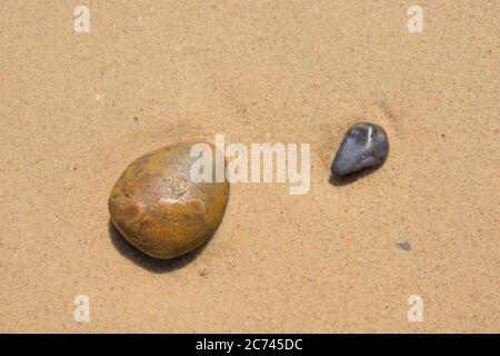 A group of pebbles pebbles resting on a background of flat water washed sand Stock Photo