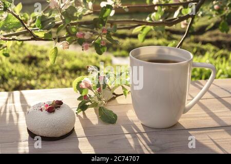 Beautiful porcelain coffee cup with mousse pastry dessert decorated with pink apple tree branches in bloom on wooden table. Spring garden in setting s Stock Photo
