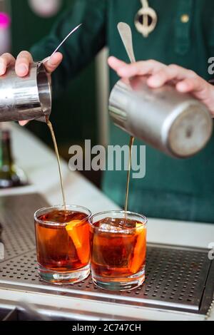 Bartender making a negroni cocktail at the bar: pouring a drink from a shaker into a glass Stock Photo