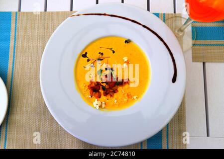 Bright yellow corn cream soup, garnished with vegetables in white plate stands on a bamboo mat. Delicious vegetarian food, a dish of vegetables and Stock Photo