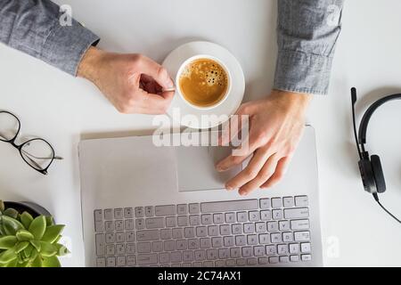 Man working on laptop and drinking coffee at his workplace. Home office, top view Stock Photo