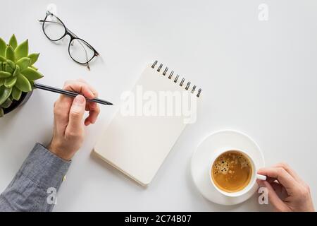 Man going to write on the empty notepad and drinking coffee at his workplace. Home office, top view. Stock Photo