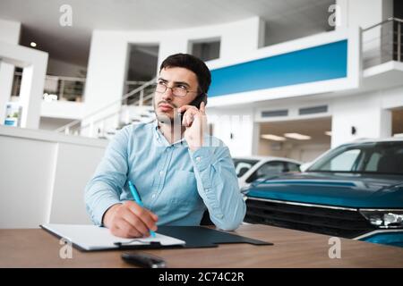 Pensive car dealership employee talking on the phone and writing Stock Photo