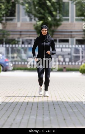 young arabian sportswoman in hijab and sportswear jogging on street Stock Photo