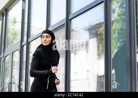 arabian girl in hijab and sportswear jogging near building Stock Photo