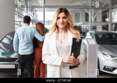 Portrait of a car sales manager woman. Auto dealership representative against the background of a couple who chooses a car Stock Photo