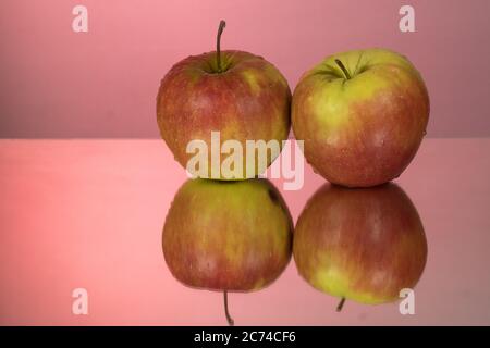 Two red apples on mirroring table on mirror red background with reflection isolated close up Stock Photo