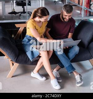 happy businessman and businesswoman using laptops while sitting on sofa Stock Photo