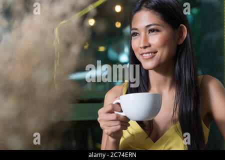 Happy young beautiful Asian woman drinking coffee and thinking at the coffee shop Stock Photo
