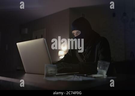 Male hacker in the hood in a dark room using computer virus program for cyber attack. Hackers and cyber security concept Stock Photo