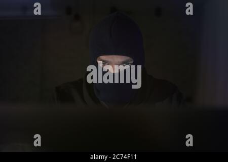 Male hacker in the hood in a dark room using computer virus program for cyber attack. Hackers and cyber security concept Stock Photo