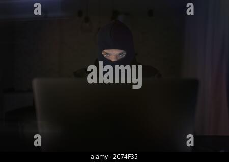 Male hacker in the hood in a dark room using computer virus program for cyber attack. Hackers and cyber security concept Stock Photo