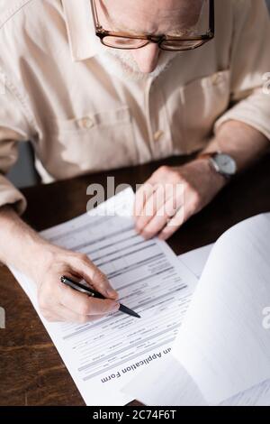 Selective focus of elderly man in eyeglasses writing on papers at table Stock Photo