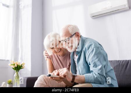 Positive senior couple using remote controller of air conditioner on sofa Stock Photo