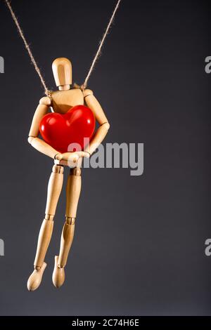 wooden marionette on strings with red heart isolated on black Stock Photo