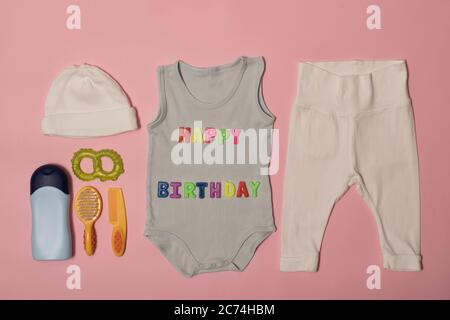 Set of clothes and accessories for newborn. Colored inscription happy birthday on a pink background. Stock Photo