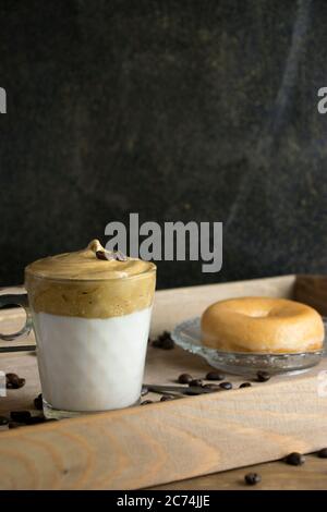 Vertical image of whipped instant coffee on top of a glass of milk with a doughnut on a wooden tray with coffee beans sprinkled. Dalgona coffee concep Stock Photo