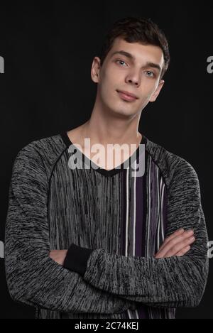 Portrait of serious young man with folded and crossing hands standing on black background Stock Photo