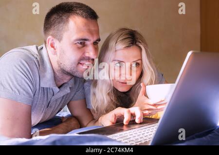 Young couple lying on the bed at home and using their laptop. Modern lifestyle. Stock Photo
