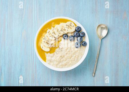 Oatmeal with bananas, blueberries, chia seeds, jam on blue wooden background. Top view. Healthy breakfast. Stock Photo