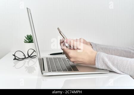 Unrecognizable woman using smartphone while typing on laptop, concept of password entry Stock Photo