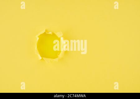 A ripped hole in yellow textured background, concept of rupted paper with copy space. Stock Photo
