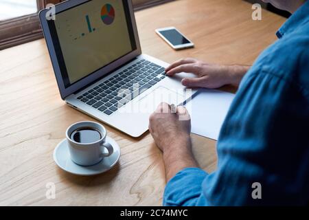 Unrecognizable man writes plan on paper and looks at charts on computer Stock Photo