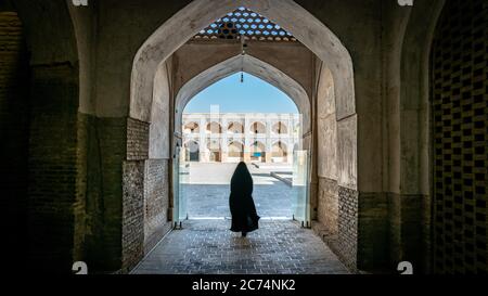 Isfahan, Iran - May 2019: Unidentified woman in hijab black dress walking towards the courtyard of the Great Mosque of Jameh Mosque of Isfahan. Stock Photo