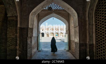 Isfahan, Iran - May 2019: Unidentified woman in hijab black dress walking towards the courtyard of the Great Mosque of Jameh Mosque of Isfahan. Stock Photo