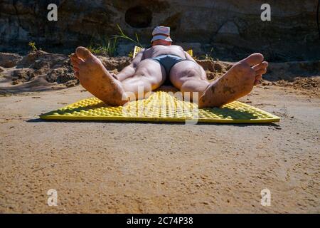 the guy in the hat and swimming trunks lies on the shore and sunbathes under the sun on the island Stock Photo