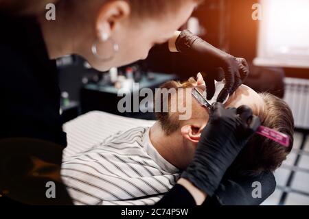 Barber shaving a man in barbershop, close up Stock Photo