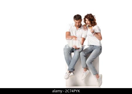 surprised woman holding credit card near man using laptop on white Stock Photo
