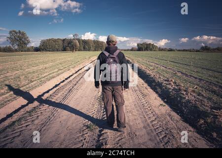 Traveler with backpack walking the dirt road, view in sunny day Stock Photo