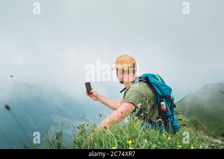 Young backpacker man taking picture of  cloudy valley bottom using smartphone during walking by the foggy cloudy weather mountain range .  Active spor Stock Photo