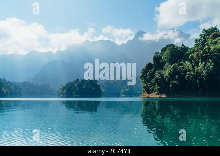 Incredible view of Cheow Lan lake with rainforest jungle on the banks with sun rays shining through white clouds. Surat Thani Province, Thailand. Stock Photo