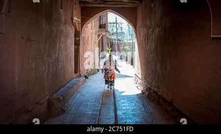 Abyaneh, Iran - May 2019: Unidentified woman with traditional Persian clothes walking down a narrow road Stock Photo