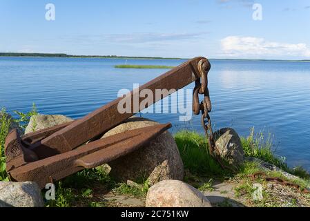 Large rusty old anchor on rocky baltic sea shore. Stock Photo