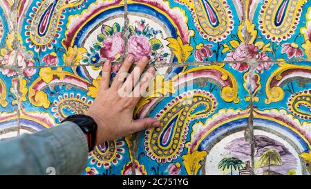 Tehran, Iran - May 2019: Hand touching colorful painting mosaic tiles on the wall at Golestan palace Stock Photo