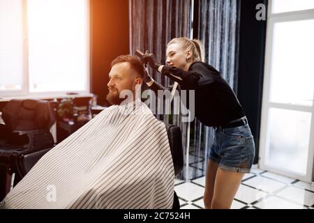 Portrait of a man in Barbershop, shave and cut by barber girl Stock Photo