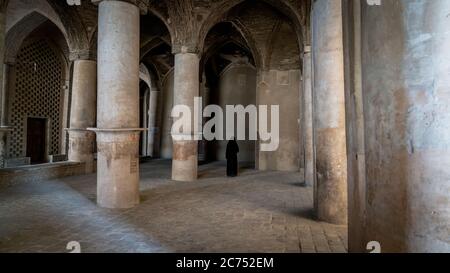 Isfahan, Iran - May 2019: Unidentified iranian woman in hijab black dress walking along the ancient columns of Jameh Mosque of Isfahan Stock Photo