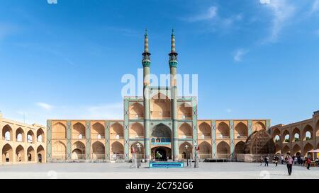 Yazd, Iran - May 2019: Jameh Mosque entrance gate with minarets with iranian people and tourists walking around Stock Photo