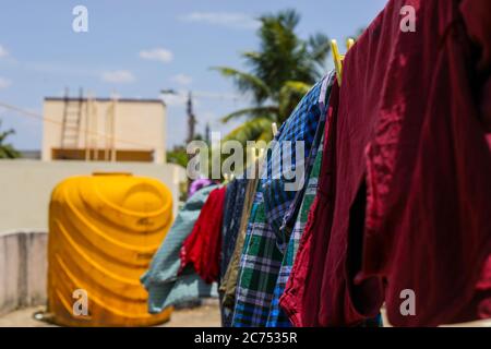Colorful clothes hanging to dry on a laundry line and sun shining in the blue sky background Stock Photo