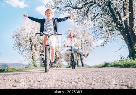 Father and son having fun spreading wide legs and screaming when riding bicycles on country road under blossom trees. Healthy sporty lifestyle concept Stock Photo