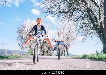 Father and son having fun spreading wide legs and screaming when riding bicycles on country road under blossom trees. Healthy sporty lifestyle concept Stock Photo