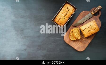 Two freshly baked homemade pumpkin bread loaves with knife over dark background. Image shot from top view, flatlay. Stock Photo