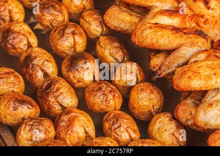 Closeup of baked jacket potatoes on a charcoal grill and chicken wings on a skewer. Fried vegetables and chicken to golden crust with spices on a stre Stock Photo