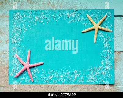 Two colored starfish and sea salt on a turquoise background. Natural material frame with place for text. Top view. Stock Photo