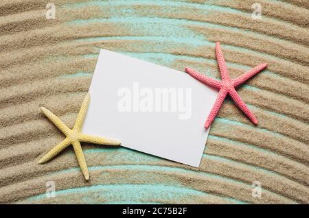 Two colored starfish on lie on texture sand. Flat lay with blank paper, place for text. Stock Photo