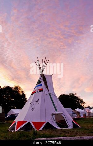 Tipi with handpainted traditional Native American cattle head art decoration in glamping field with at a festival campsite at sunset, Norfolk Stock Photo