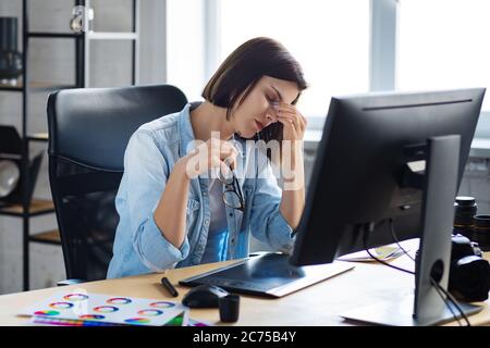Portrait of tired graphic designer working overtime in office. Stressed worker have eye strain symptoms. Retoucher workplace in photo studio. Burnout Stock Photo